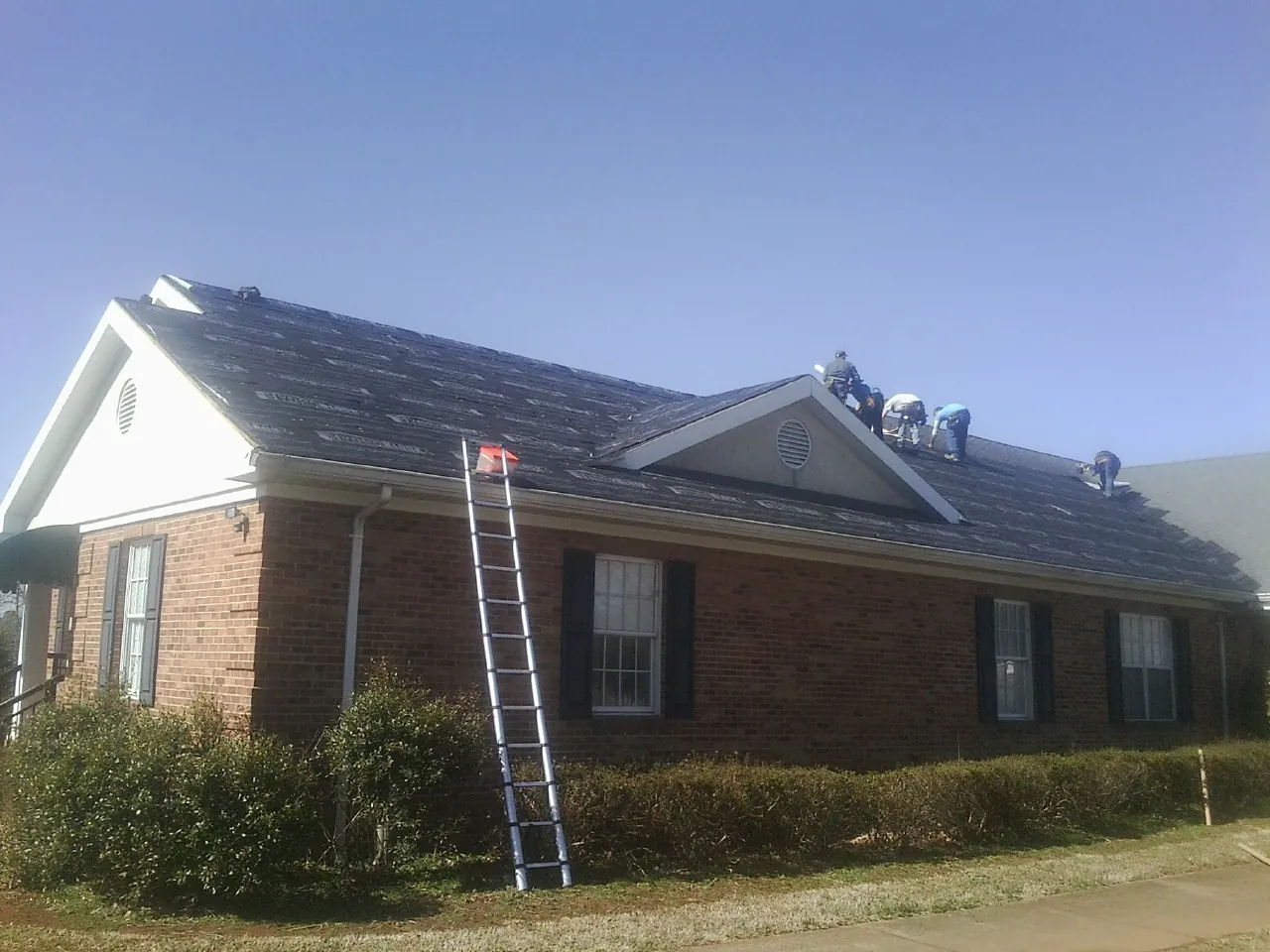 Crew tearing shingles off a brick ranch roof with a ladder set — Metal Roof Repair work by our crew in Temple