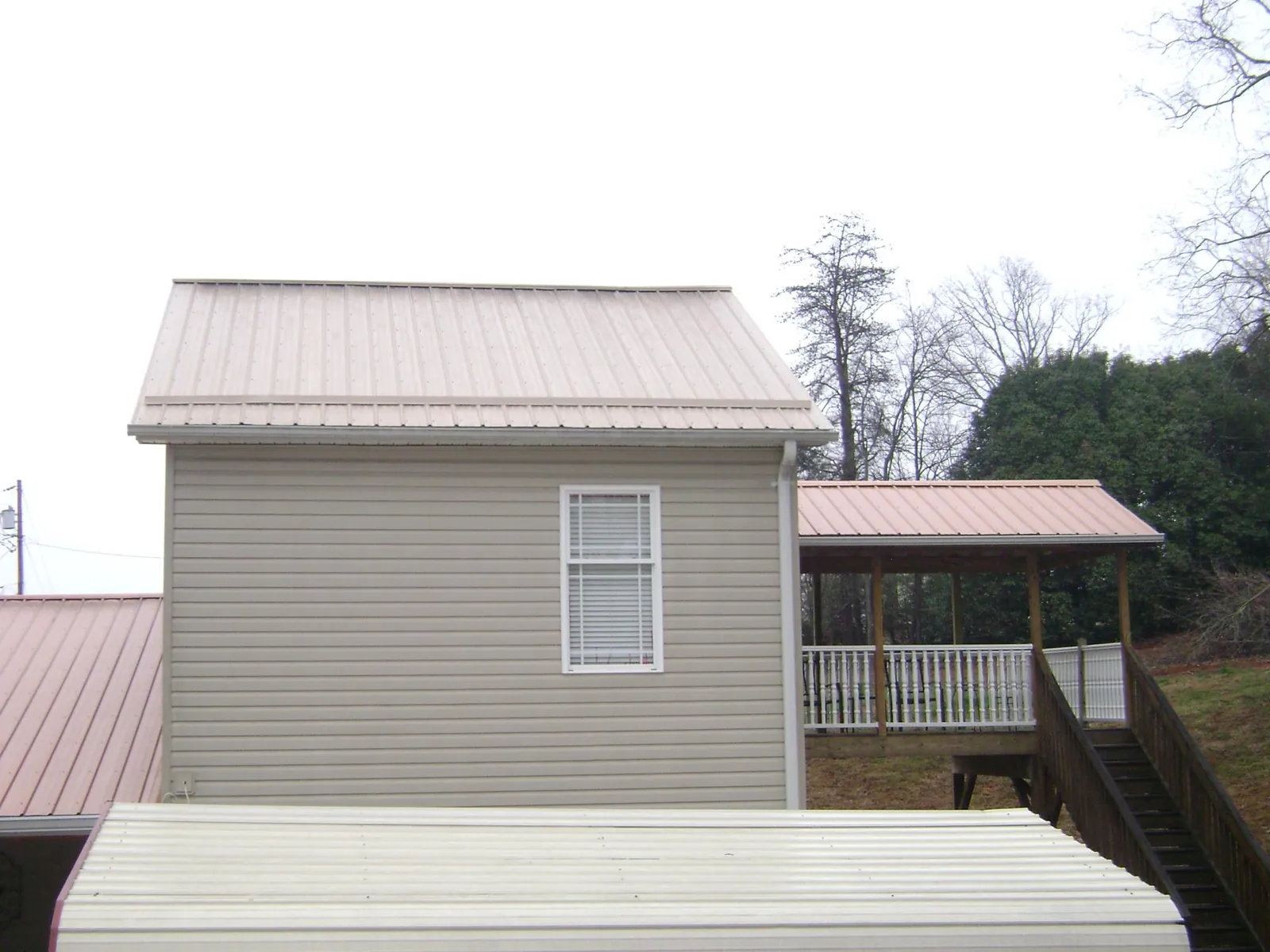 Tan metal roofs on a two story addition and attached porch, from a Roof Replacement job in Temple